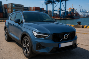 Volvo XC40 azul denim de 2023 estacionado en una terminal portuaria junto a documentos administrativos, ilustrando las dificultades para exportar un coche con cargas.